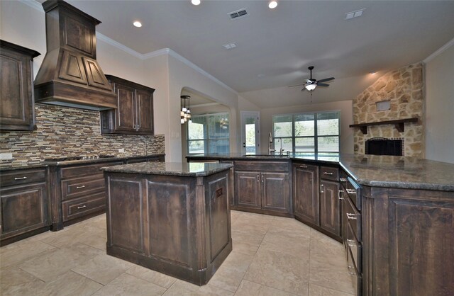 kitchen featuring premium range hood, dark brown cabinetry, a center island, and ceiling fan with notable chandelier