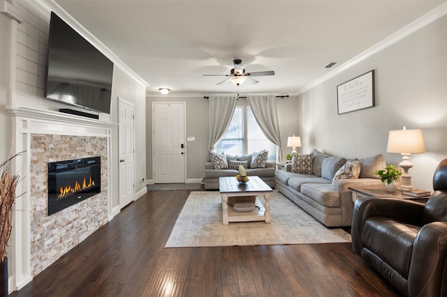 living room with a stone fireplace, ornamental molding, dark wood-type flooring, and ceiling fan