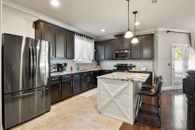 kitchen with dark brown cabinets, appliances with stainless steel finishes, pendant lighting, crown molding, and a center island