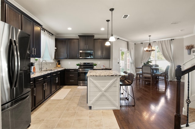 kitchen with a center island, hanging light fixtures, stainless steel appliances, ornamental molding, and light hardwood / wood-style flooring