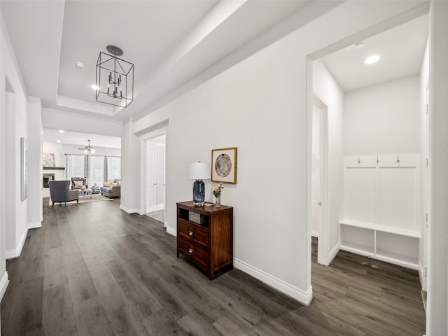 hallway featuring dark wood-type flooring, a tray ceiling, recessed lighting, baseboards, and a chandelier