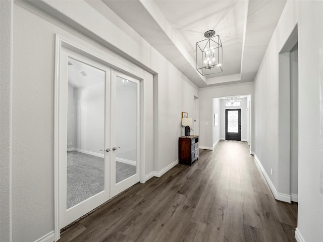 hall featuring french doors, a raised ceiling, baseboards, and dark wood-style flooring