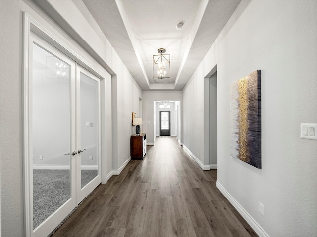 hallway with baseboards, dark wood finished floors, french doors, a notable chandelier, and a raised ceiling