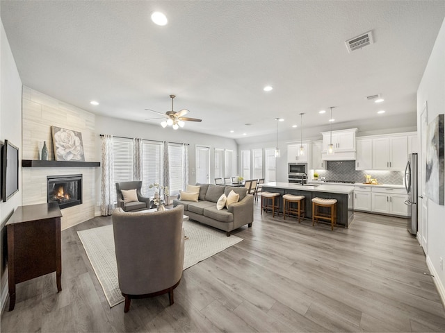 living area with recessed lighting, visible vents, light wood-style floors, and a tile fireplace