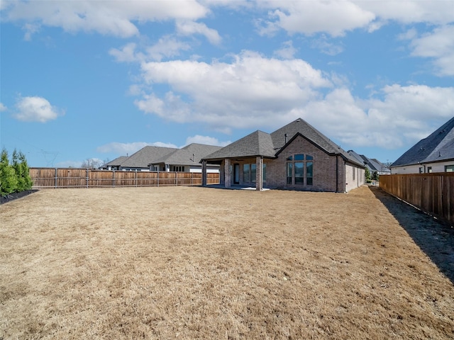 rear view of property featuring brick siding, a lawn, and a fenced backyard