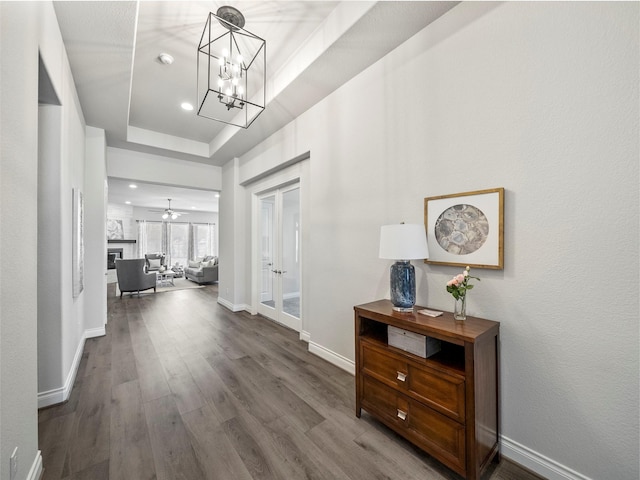 hallway featuring a tray ceiling, baseboards, wood finished floors, and french doors