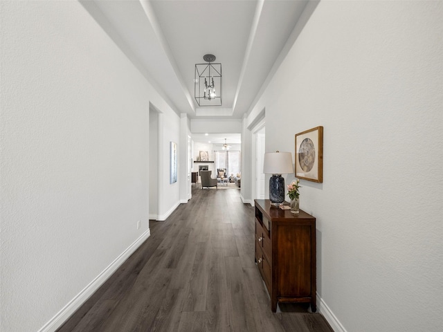 hallway with dark wood-style floors, a raised ceiling, and baseboards