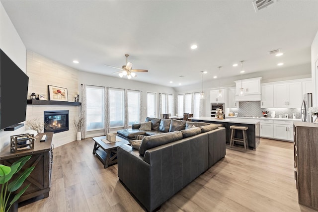 living room with a tiled fireplace, ceiling fan, and light hardwood / wood-style floors