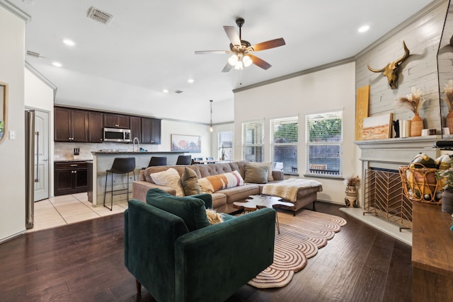 living room with light hardwood / wood-style flooring, ceiling fan, crown molding, and sink