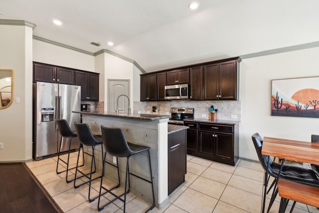 kitchen featuring a kitchen bar, appliances with stainless steel finishes, dark brown cabinets, and a kitchen island with sink