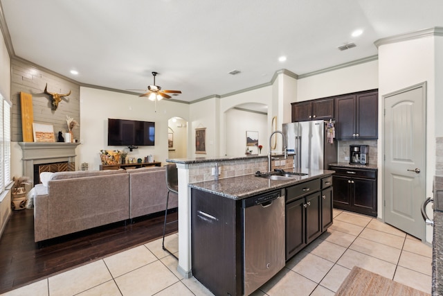 kitchen with a center island with sink, light tile patterned floors, ornamental molding, appliances with stainless steel finishes, and dark brown cabinetry