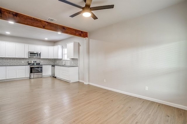 kitchen with appliances with stainless steel finishes, white cabinets, beam ceiling, and light wood-type flooring