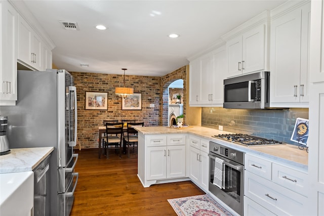 kitchen featuring kitchen peninsula, dark hardwood / wood-style flooring, white cabinetry, decorative light fixtures, and stainless steel appliances