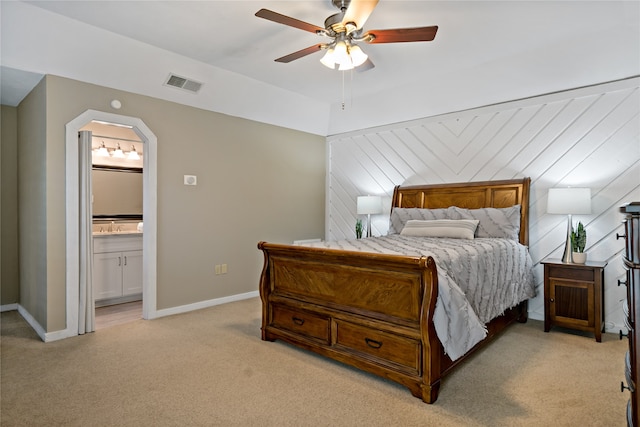 carpeted bedroom with ensuite bath, wooden walls, and ceiling fan