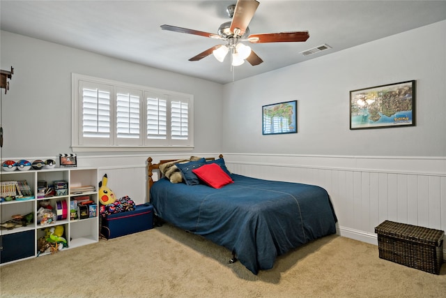 bedroom with light carpet, wooden walls, and ceiling fan