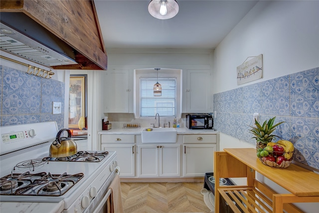 kitchen featuring white gas range oven, custom range hood, sink, pendant lighting, and white cabinetry