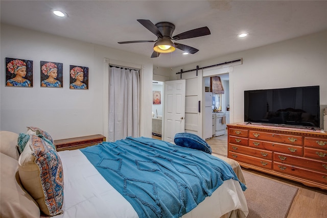 bedroom with a barn door, light hardwood / wood-style floors, ensuite bath, and ceiling fan