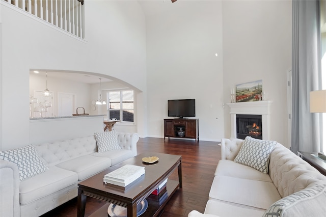 living room featuring a towering ceiling, dark wood-type flooring, and an inviting chandelier