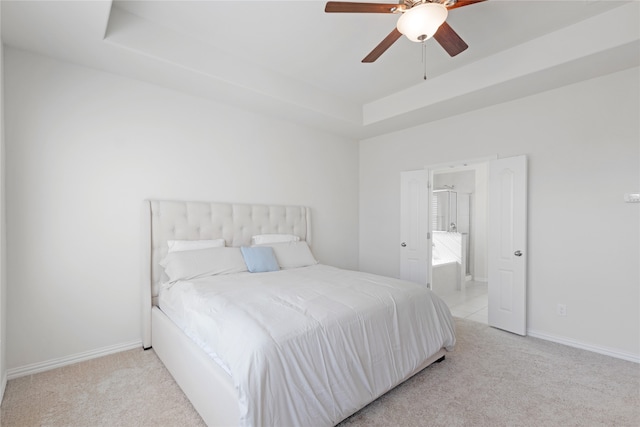 carpeted bedroom with ceiling fan, ensuite bath, and a tray ceiling