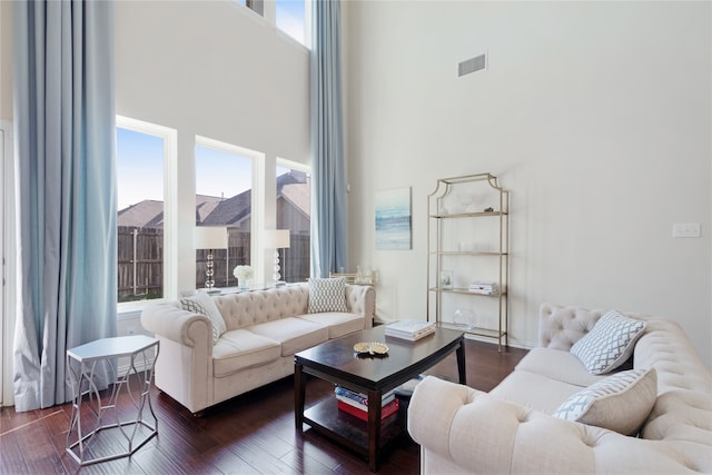 living room with a towering ceiling and dark wood-type flooring