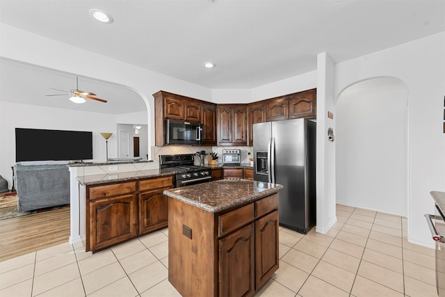 kitchen with light tile patterned flooring, ceiling fan, dark brown cabinets, a kitchen island, and stainless steel appliances