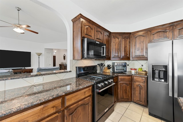 kitchen featuring decorative backsplash, appliances with stainless steel finishes, ceiling fan, dark stone countertops, and light tile patterned flooring