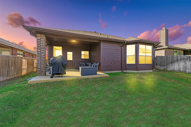 back house at dusk with a lawn and a patio