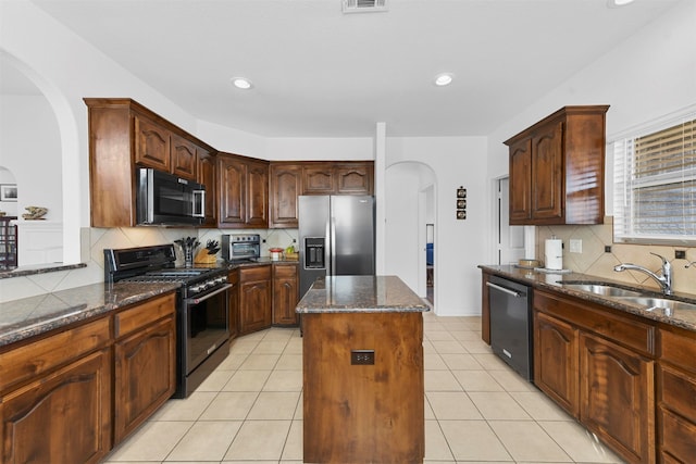 kitchen with sink, light tile patterned floors, dark stone countertops, a kitchen island, and appliances with stainless steel finishes