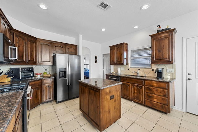 kitchen featuring sink, stainless steel appliances, dark stone countertops, decorative backsplash, and a kitchen island