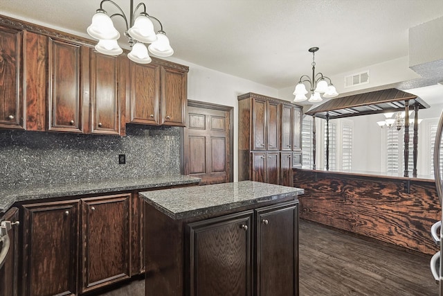 kitchen with dark brown cabinetry, dark stone counters, an inviting chandelier, and dark hardwood / wood-style flooring