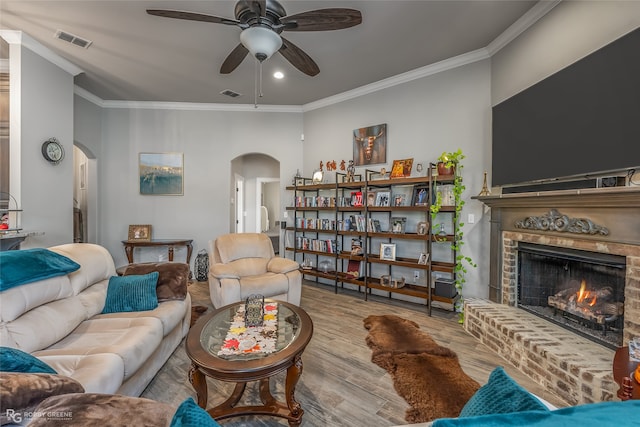 living room featuring crown molding, ceiling fan, a fireplace, and light wood-type flooring