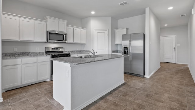 kitchen with appliances with stainless steel finishes, white cabinetry, a kitchen island with sink, light stone countertops, and sink