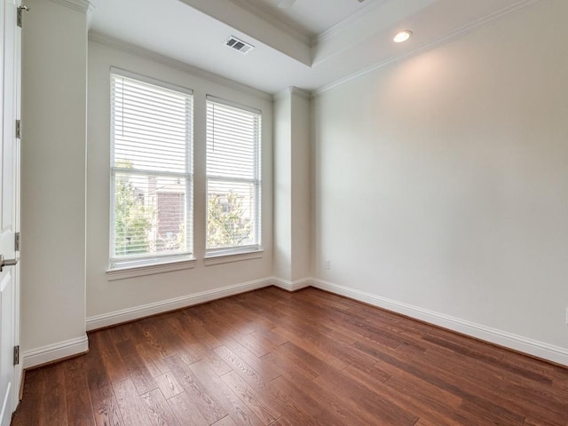 empty room with a tray ceiling, crown molding, and dark wood-type flooring