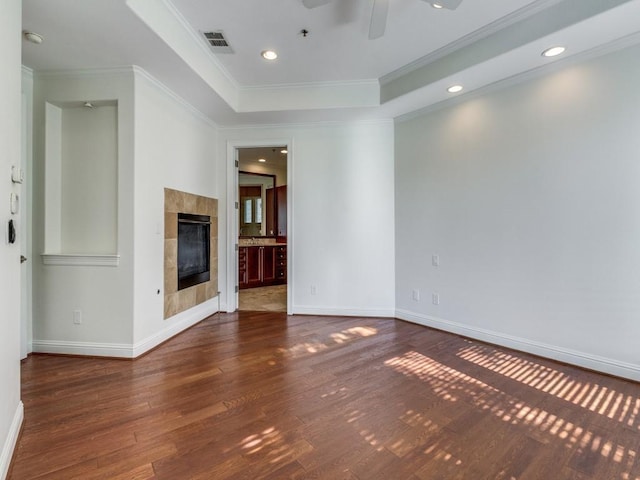 unfurnished living room with a fireplace, a tray ceiling, dark wood-type flooring, and ornamental molding