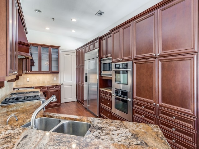 kitchen with sink, light stone counters, tasteful backsplash, built in appliances, and dark hardwood / wood-style flooring