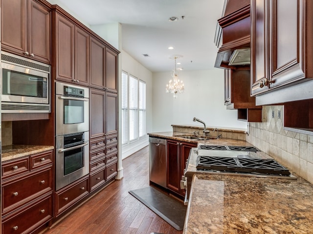 kitchen featuring stone counters, sink, dark hardwood / wood-style flooring, stainless steel appliances, and decorative light fixtures