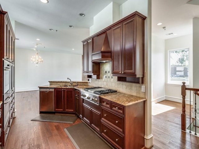 kitchen with appliances with stainless steel finishes, sink, hanging light fixtures, custom exhaust hood, and light stone counters