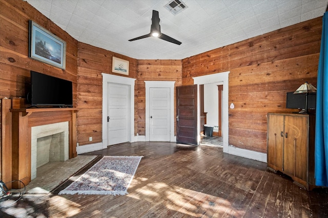 unfurnished living room featuring dark wood-type flooring, ceiling fan, a high end fireplace, and wood walls