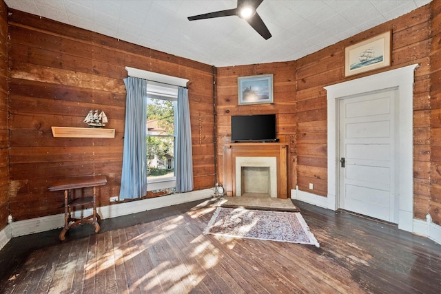 living room featuring dark wood-type flooring, wooden walls, and ceiling fan