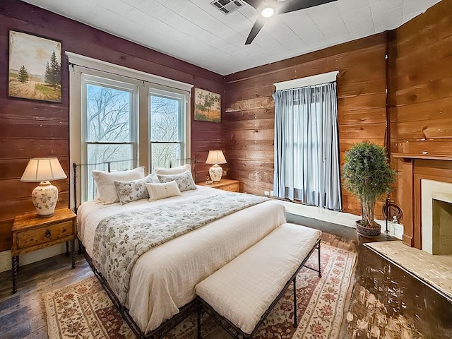 bedroom featuring dark hardwood / wood-style flooring, wooden walls, and ceiling fan