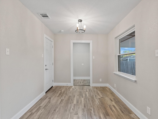 empty room with a notable chandelier, a textured ceiling, and light wood-type flooring