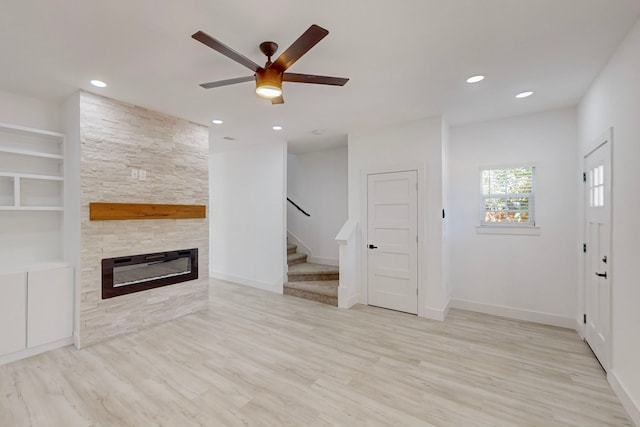 unfurnished living room featuring ceiling fan, a stone fireplace, and light hardwood / wood-style flooring