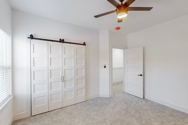 unfurnished bedroom featuring a barn door, light carpet, a closet, and ceiling fan