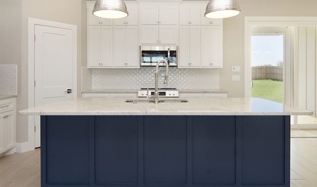 kitchen featuring a center island with sink, white cabinetry, light stone counters, and pendant lighting