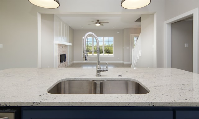 kitchen with sink, light stone countertops, a fireplace, and ceiling fan