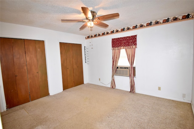 unfurnished bedroom featuring carpet flooring, a textured ceiling, cooling unit, ceiling fan, and two closets