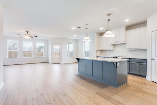 kitchen featuring white cabinets, an island with sink, open floor plan, decorative light fixtures, and a sink