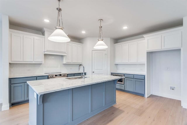 kitchen with hanging light fixtures, a center island with sink, white cabinets, and a sink