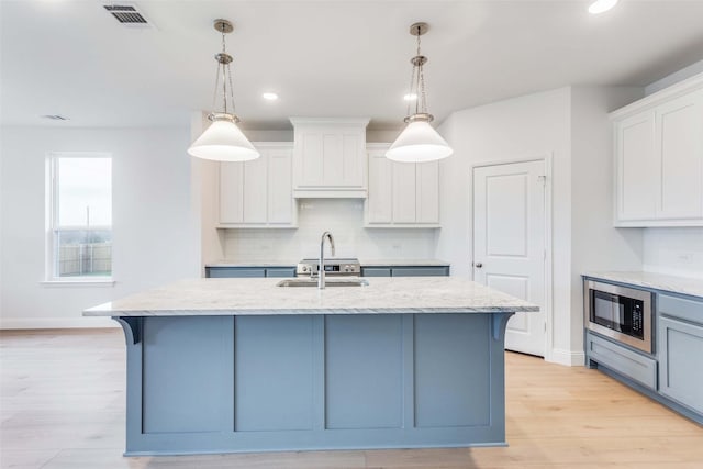 kitchen with black microwave, white cabinets, a center island with sink, and a sink