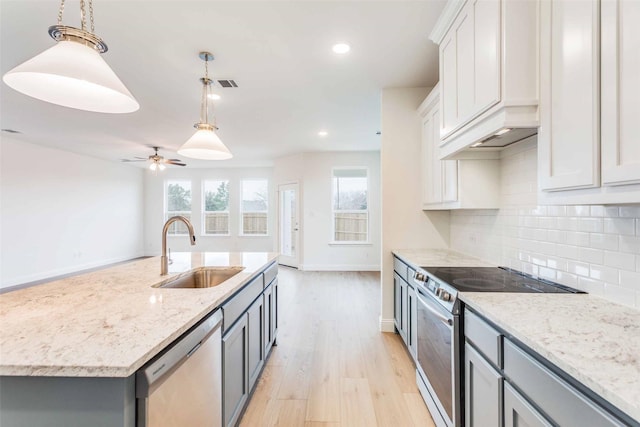 kitchen featuring pendant lighting, stainless steel appliances, white cabinets, a sink, and an island with sink